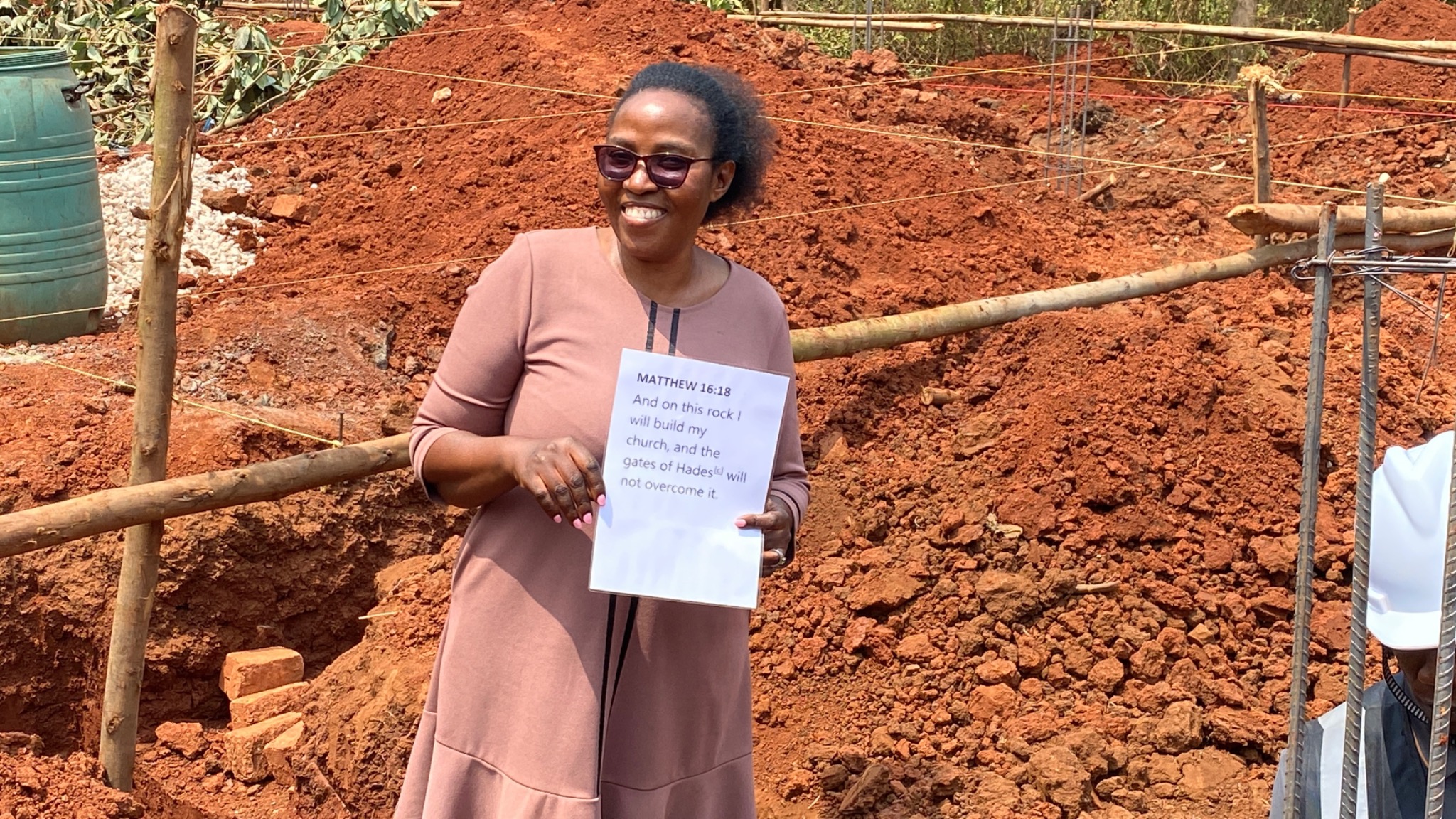 A woman at the foundation site holds a sign with the words of Matthew 16:18.