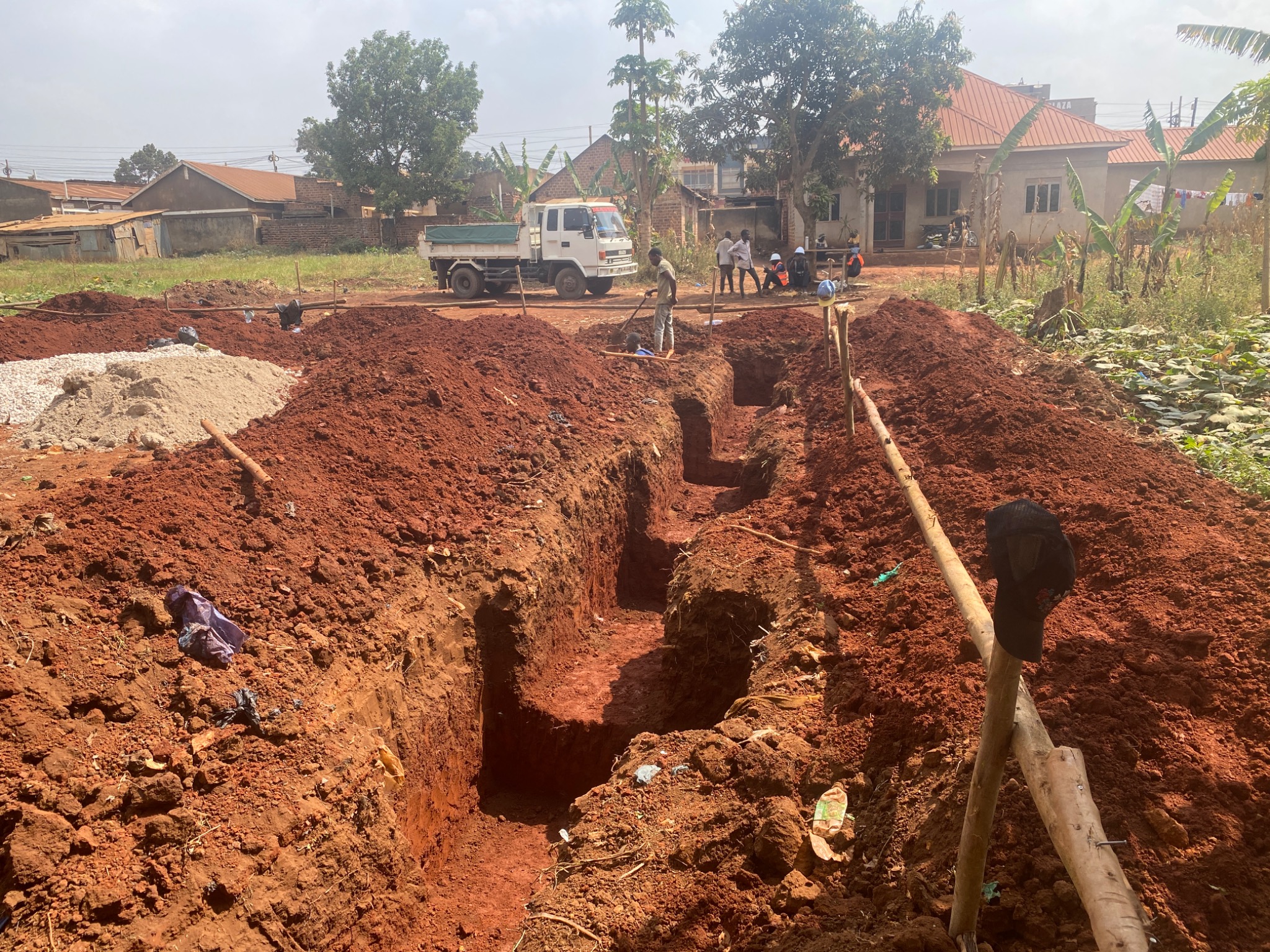 Foundation trenches being dug at the Shalom House site, with workers and building materials nearby.